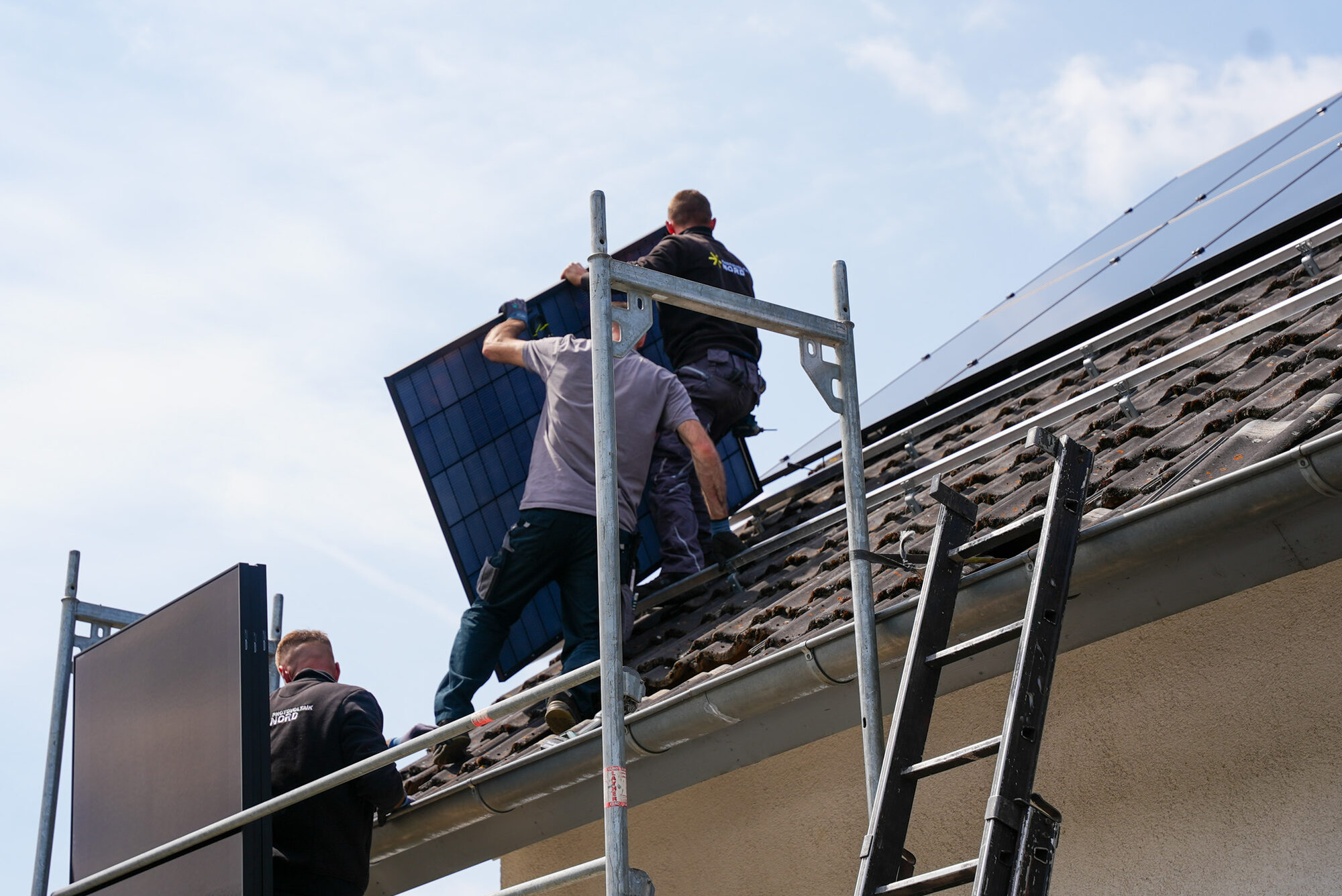 Monteure tragen ein Solarmodul auf das Dach